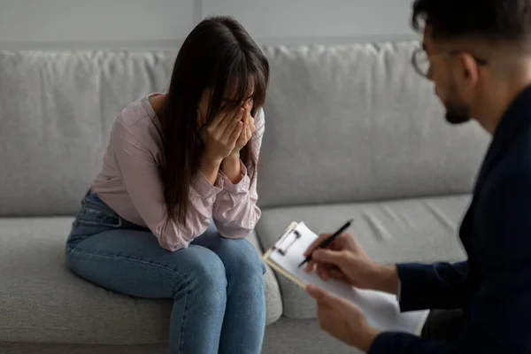 Male psychologist talking to crying lady during therapy session, giving advices to depressed arab woman