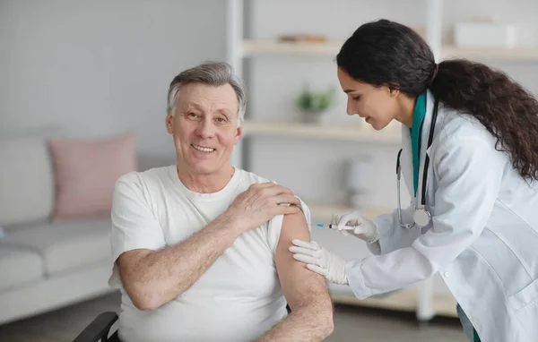 Junger Arzt spritzt Senioren im Rollstuhl zu Hause Medikamente oder Anti-Covid-Impfstoff — Stockfoto