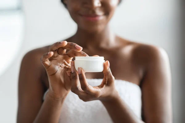 Tarro con loción corporal en irreconocible mano de dama afroamericana — Foto de Stock