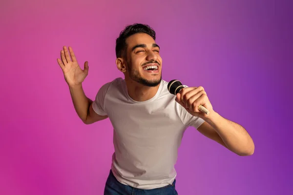 Porträtt av cool ung arabisk man sång, med hjälp av mikrofon, utför karaoke i neonljus — Stockfoto