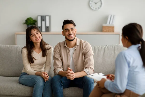 Familjeterapi. Glada mellanösternpar sitter på soffan på rådgivningsbyrån, lyssnar på råd och ler — Stockfoto