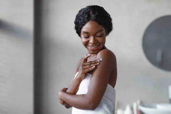 Sensuele Afrikaanse Amerikaanse jonge vrouw met behulp van huidverzachter, badkamer interieur — Stockfoto