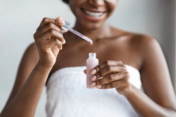 Mujer negra irreconocible sosteniendo botella con producto de belleza —  Fotos de Stock