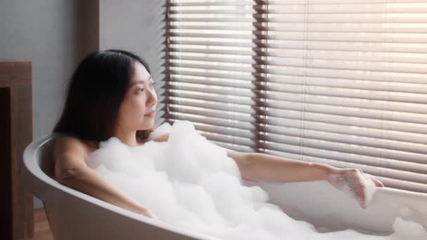 Güzel Asyalı kadın banyo köpükleriyle küvette uzanıyor, lüks banyoda dinleniyor. — Stok video