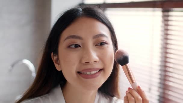 Makyaj. Güzel Asyalı kadın makyaj fırçasıyla yanaklarına allık sürüyor. — Stok video