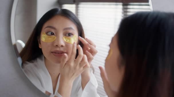 Güzel Asyalı kadın banyoda aynanın yanında dikilirken göz altı bantları yapıştırıyor. — Stok video