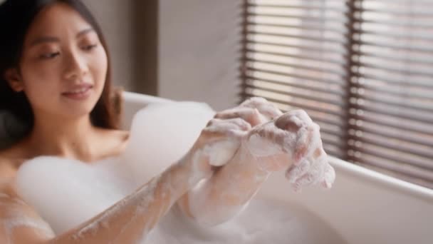 Linda asiática feminina lavar as mãos com sabão de banho enquanto relaxa na banheira — Vídeo de Stock