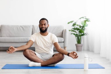 Huzurlu, sakin, bin yıllık Afro-Amerikan sakallı erkek yoga yapıyor. Yerde gözleri kapalı.
