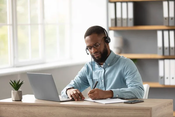 Druk bezig serieuze millennial afrikaanse amerikaanse baardman in bril en headset werken op laptop in huis — Stockfoto