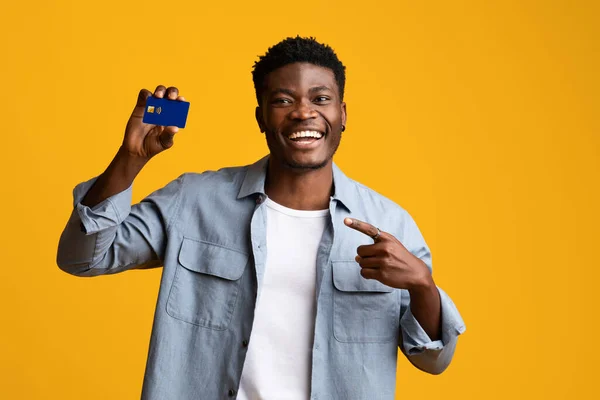 Happy black guy showing credit card on yellow — Stock Photo, Image
