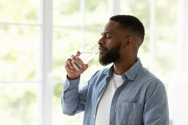 Calma bello millenario africano americano barbuto ragazzo bere acqua limpida ogni giorno su sfondo finestra, profilo — Foto Stock