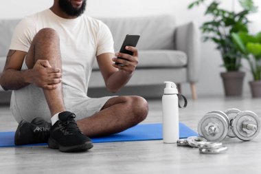 Kırpılmış milenyum Afrikalı Amerikalı adam yerde yatıyor. İç tarafta halterler ve şişelerle.