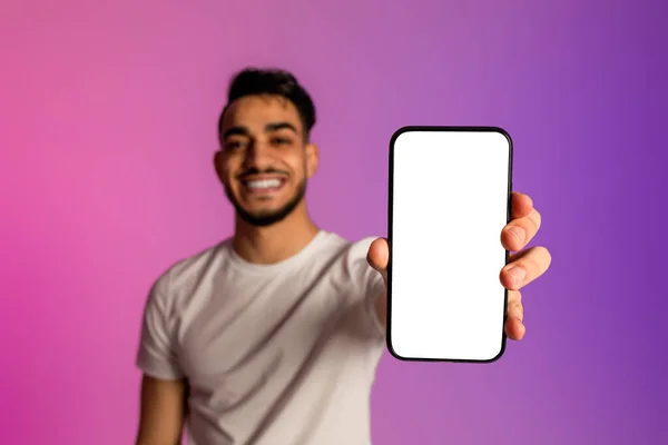 Jeune homme arabe souriant montrant smartphone avec écran blanc, recommandant site Web ou annonce dans la lumière au néon, maquette — Photo