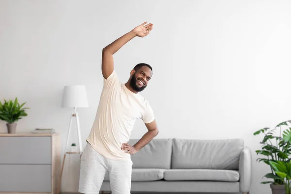 Felice giovane uomo afroamericano con la barba in abbigliamento sportivo bianco facendo esercizio fisico e riscaldamento — Foto Stock