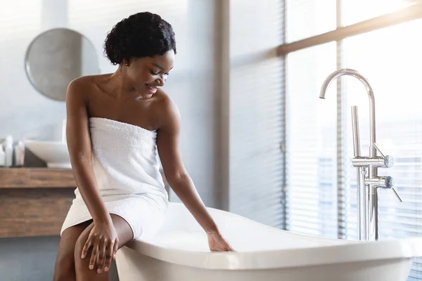 Positieve aantrekkelijke zwarte dame zitten op bad in moderne badkamer — Stockfoto