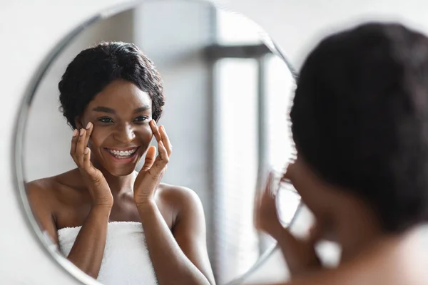 Reflejo del espejo de la señora negra feliz aplicando el producto del cuidado del ojo — Foto de Stock