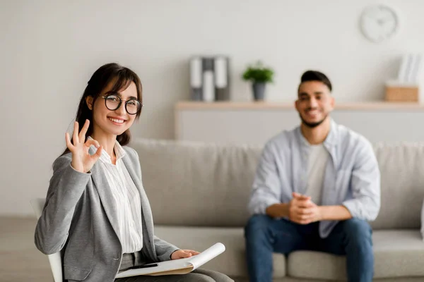 Successful therapy. Professional young female psychologist gesturing okay sign working with millennial arab man — Stock Photo, Image