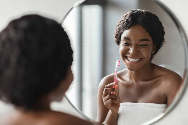 Svart kvinna borstar tänderna och ler i badrummet — Stockfoto
