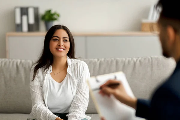 Succesvolle psychotherapie. Happy arab vrouwelijke cliënt met sessie met psycholoog, glimlachen, zitten op de bank in kliniek — Stockfoto