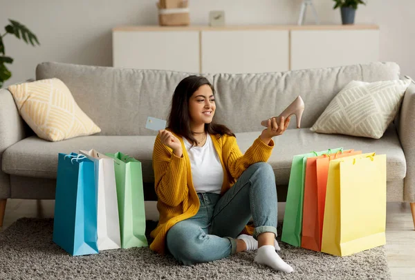 Kolay ödeme, uzaktan alışveriş. Kredi kartı ve yeni ayakkabı taşıyan mutlu Arap kadın alışveriş torbalarının arasında oturuyor. — Stok fotoğraf