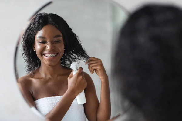 Feliz joven mujer negra usando spray para el cabello — Foto de Stock