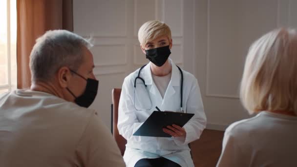 Médico feminino conversando com casal sênior vestindo máscaras de rosto interior — Vídeo de Stock