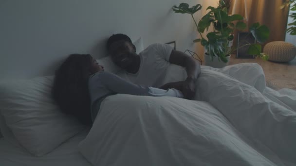 Rodinná komunikace. Mladý šťastný africký americký pár zamilovaný v pyžamu spolu mluví, leží v posteli — Stock video