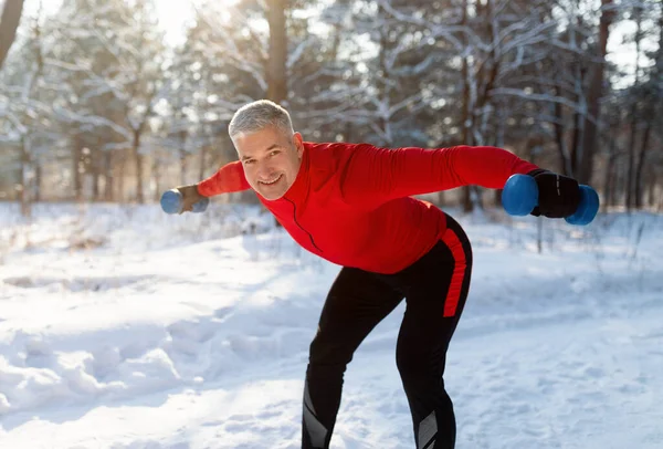 Fit старший спортсмен с гантелями делать пауэрлифтинговые упражнения в снежном парке. Зимняя тренировка на открытом воздухе — стоковое фото