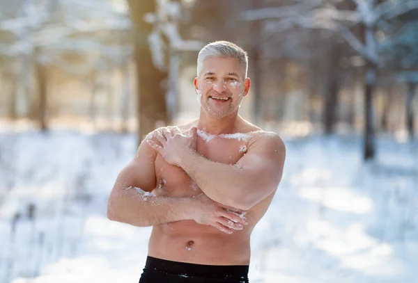 Позитивный пожилой человек закаляет свое тело снегом в морозном зимнем лесу. Обучение холодному воздействию — стоковое фото