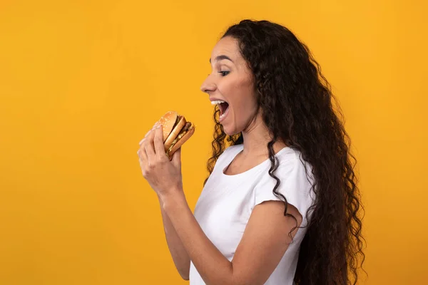 Engraçado latina senhora segurando hambúrguer mordendo sanduíche no estúdio — Fotografia de Stock