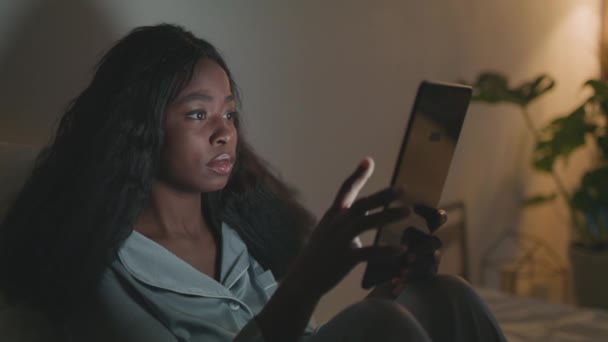 Sömnlöshet och gadgetberoende. Ung afrikansk amerikansk kvinna i pyjamas webb surfa på digital tablett sent på natten — Stockvideo