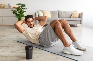 Atletik bin yıllık Arap adam yoga minderi üzerinde egzersiz yapıyor, evde karın kaslarını güçlendiriyor, tam boy.