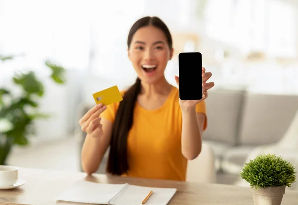Εφαρμογή για κινητά. Ενθουσιασμένη Ασιάτισσα γυναίκα δείχνει το τηλέφωνο κενή οθόνη και πιστωτική κάρτα, ψώνια σε απευθείας σύνδεση από το σπίτι — Φωτογραφία Αρχείου
