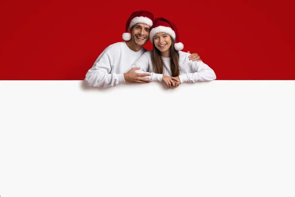 Annonce du Nouvel An. Couple heureux portant chapeaux Santa penché au tableau blanc — Photo