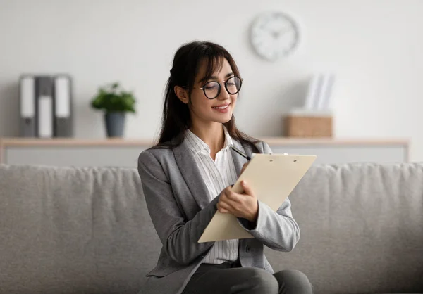 Gericht Arabisch vrouwelijke psycholoog zitten op de bank en schrijven in klembord, het aanbieden van professionele counseling diensten — Stockfoto