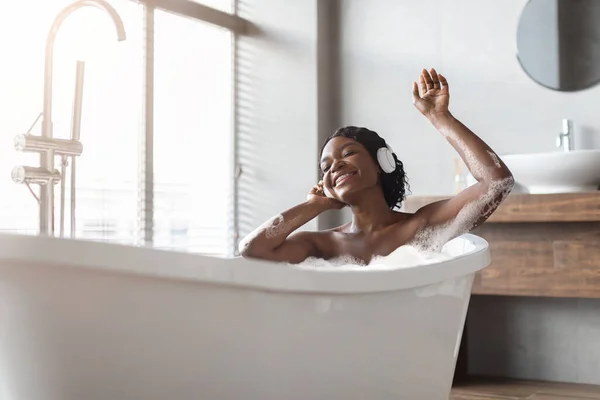 Позитивная американка из Африки принимает пенную ванну и слушает музыку. — стоковое фото