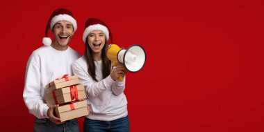 Tatil tanıtımı. Neşeli çift Noel Baba Şapka Giyiyor Megafon ve Hediye Kutuları Tutuyor