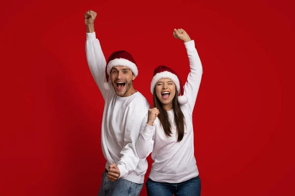 Святкування Різдва. Задоволені парою в Санта - Капелюхах, які відзначають успіх з піднятими кулаками — стокове фото