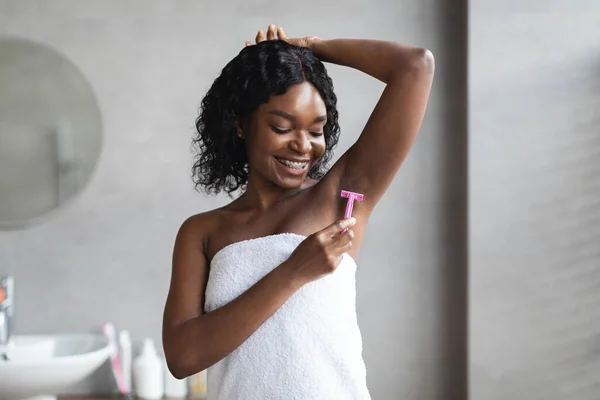 Lächelnde junge schwarze Frau rasiert Achselhöhlen im Badezimmer — Stockfoto