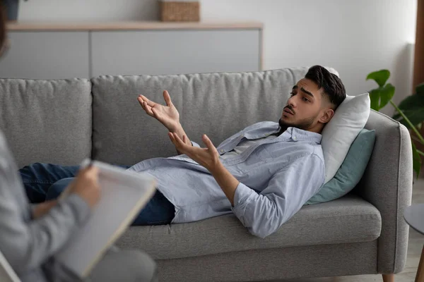 Hombre árabe deprimido acostado en el sofá en la oficina de psicólogos, teniendo una sesión con el consejero, buscando ayuda profesional — Foto de Stock