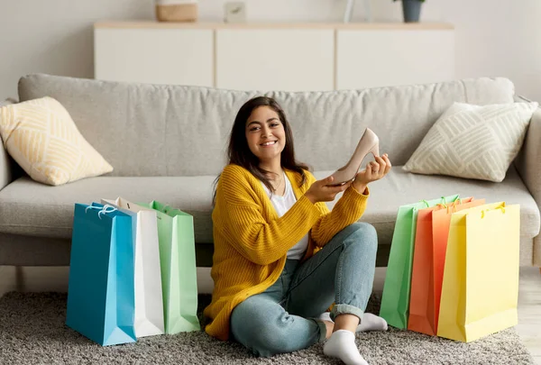 Yeni ayakkabısı olan mutlu bir orta doğulu kadın, renkli alışveriş torbalarının arasında oturuyor ve kameraya gülümsüyor. — Stok fotoğraf