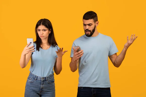 Нет WiFi. Разочарованные ближневосточные супруги со смартфонами, страдающие проблемами с интернетом, желтый фон — стоковое фото