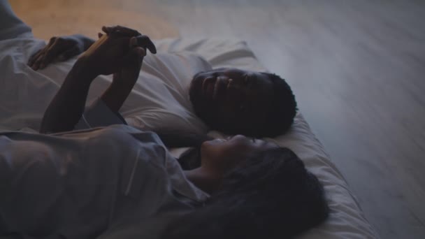 Kärlek och enhet. Närbild av unga glada älskande afrikanskt amerikanskt par hålla händer och skratta i sängen, spåra skott — Stockvideo