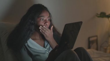 Şok edici bir haber. Genç uykusuz Afrikalı Amerikalı kadın pijama giyiyor sosyal medya okuyor ve şok geçiriyor.