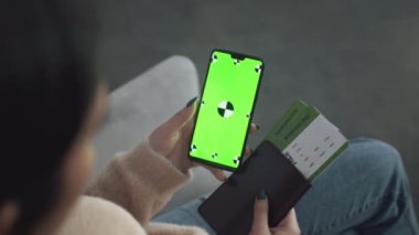Uçuş biletleri olan tanınmayan bir kadın mobil uygulamayı kontrol ediyor. Cep telefonu yeşil renkli ekran.