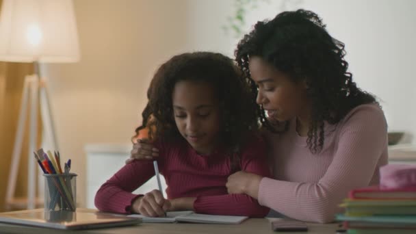 Amoroso afro-americano mãe ajudando filha com hometask, pequena menina negra escrevendo em livro em casa, zoom em — Vídeo de Stock