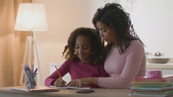 Orgulhoso dos pais. Cuidar da mãe afro-americana ajudando sua filha com lição de casa, beijando e abraçando seu filho inteligente — Vídeo de Stock