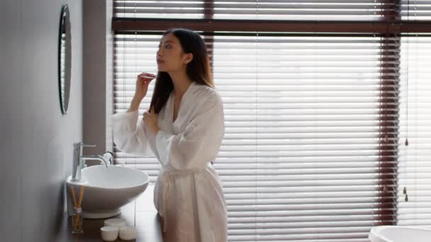 Concepto de cuidado del cabello. hermosa asiático mujer cepillado su cabello con peine en cuarto de baño — Vídeos de Stock