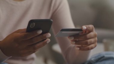 Mobil bankacılık konsepti. Tanımlanamayan siyah kadın elinde akıllı telefon ve kredi kartı tutuyor ve internet üzerinden ödeme yapıyor.