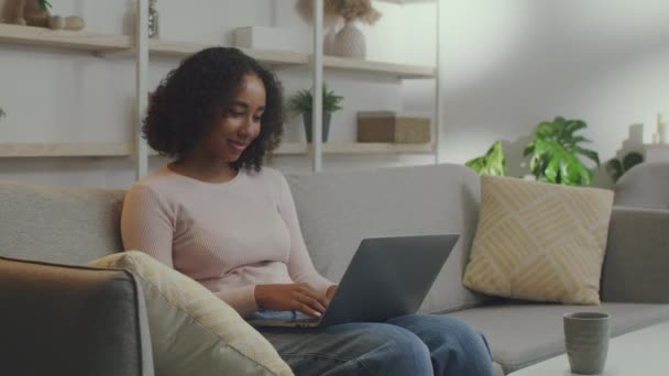 Концепція виграшу онлайн. Молода афроамериканка, яка працює на ноутбуці і читає чудові новини вдома, вільне місце. — стокове відео